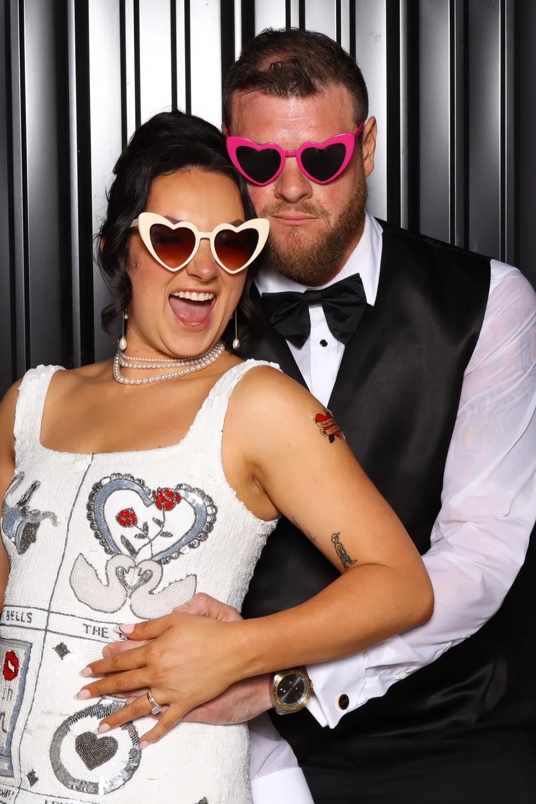 A couple in heart sunglasses posing in front of the black slat backdrop