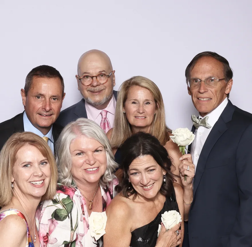 A group of guests posing together against a crisp white backdrop, holding white roses
