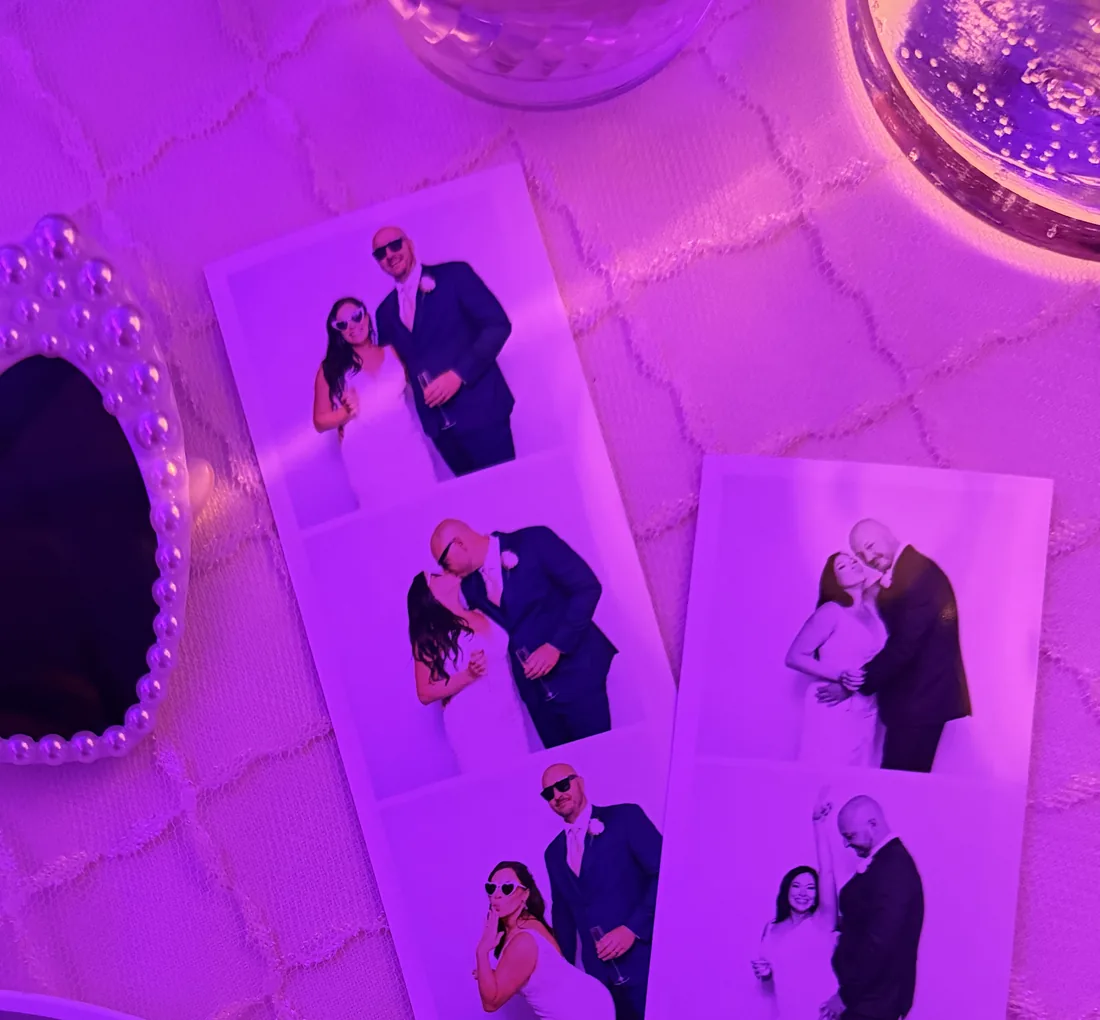 Film strip prints from the photo booth spread across a reception table under purple lighting