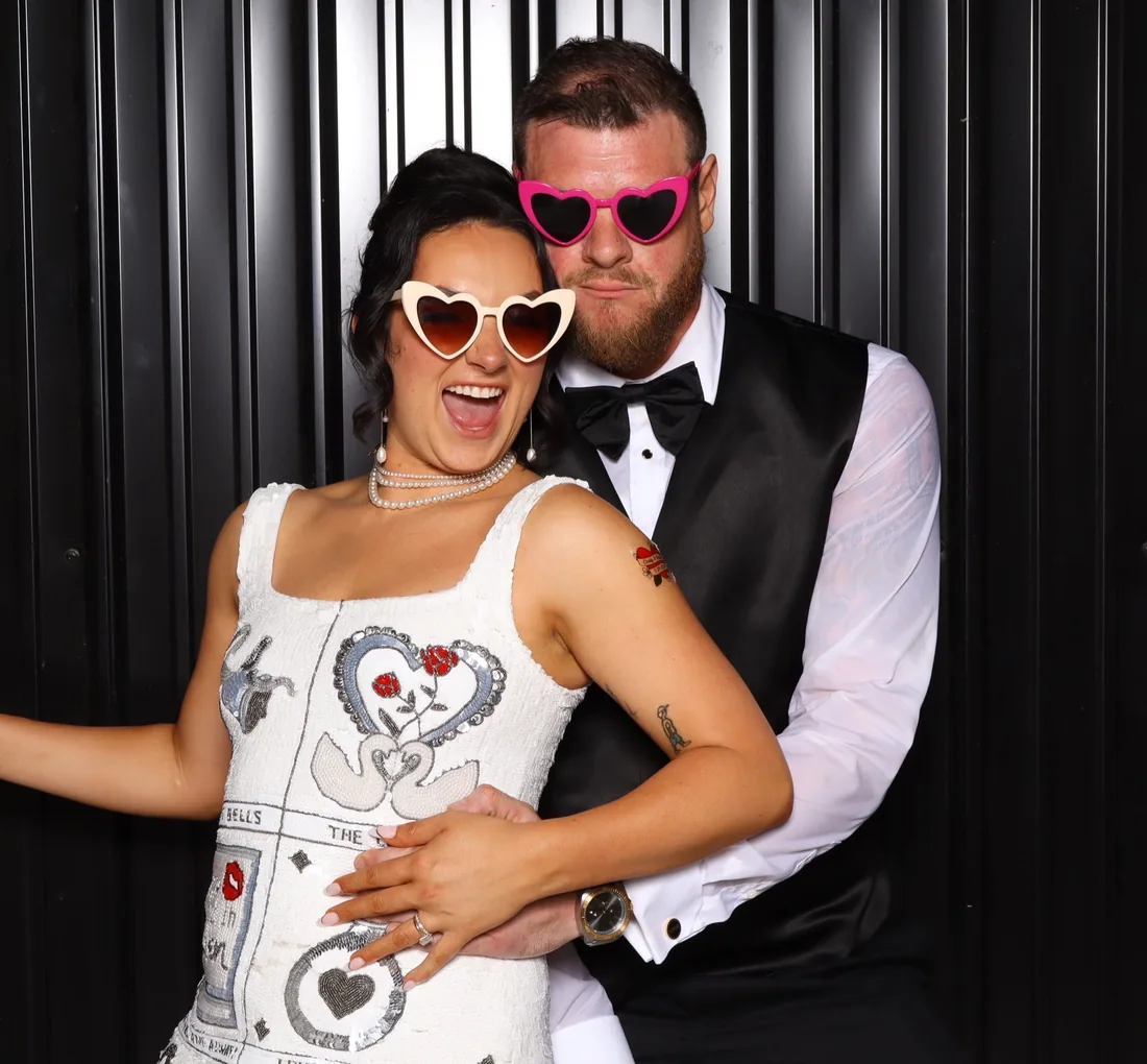 A couple in heart sunglasses posing in the photo booth against a black backdrop