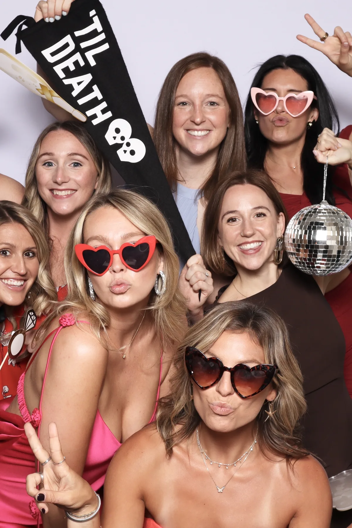 A crowd of friends with a til death banner and disco ball filling the booth frame