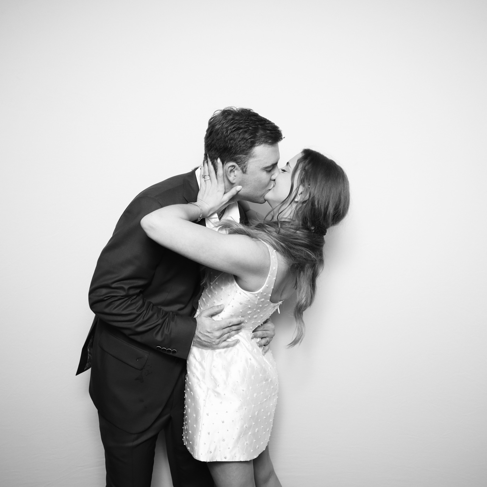 A couple kissing against a plain backdrop in a black and white glam booth portrait