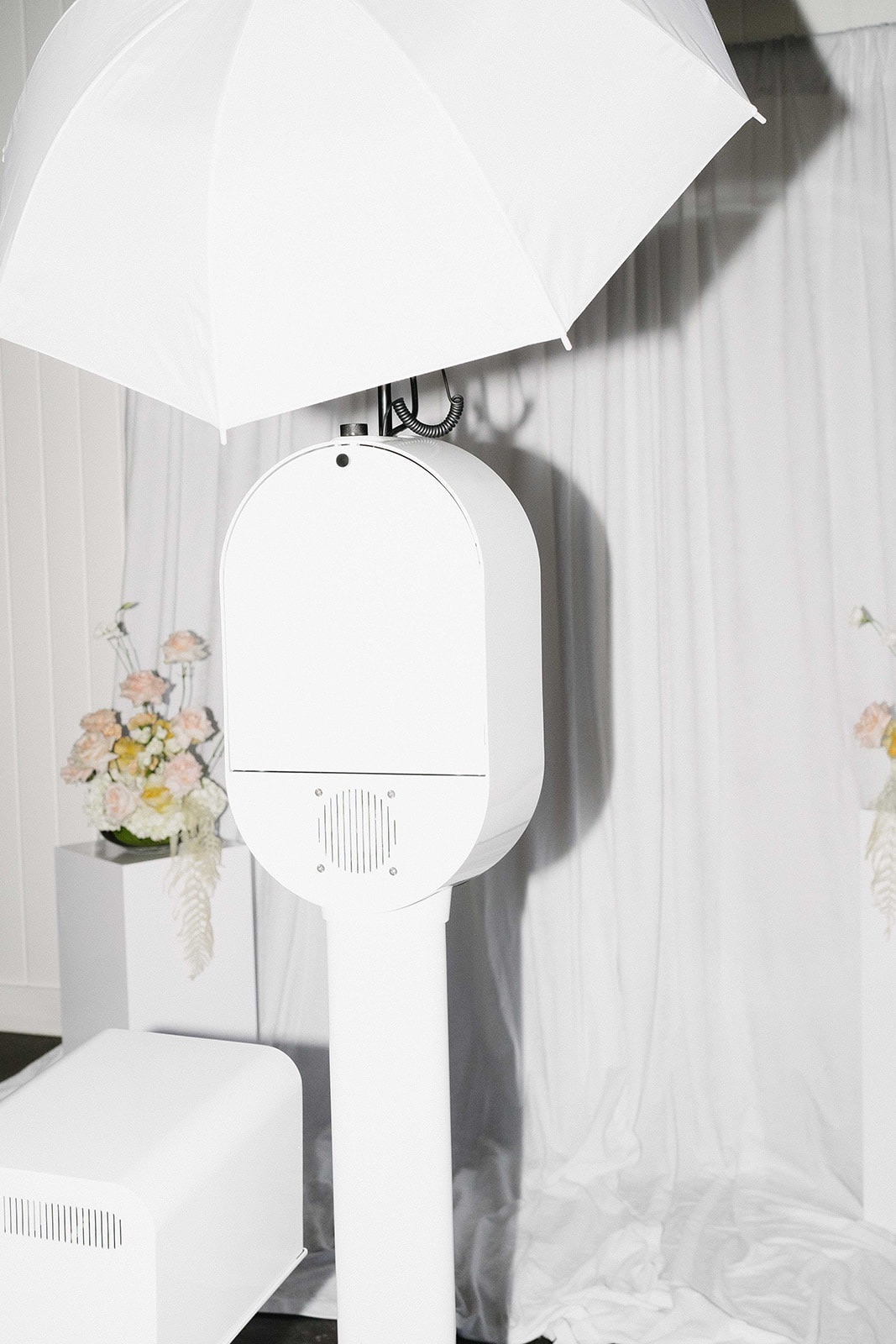 The white open air booth and printer set up beside draping and pale flowers