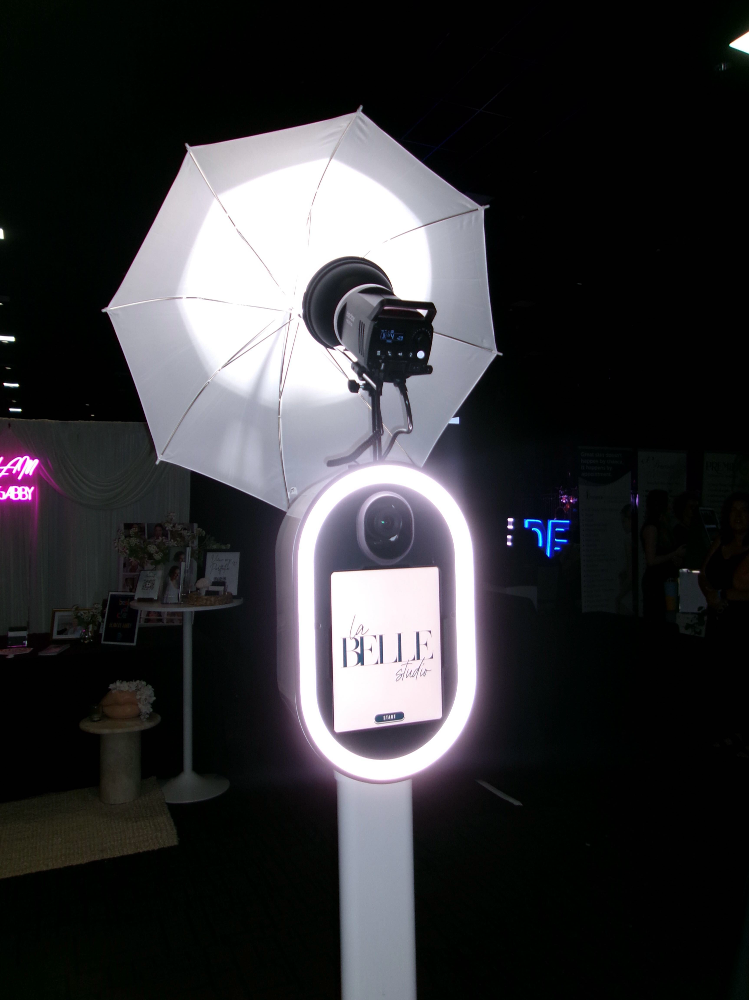 An open air booth lit by a studio umbrella, showing custom event branding on its screen