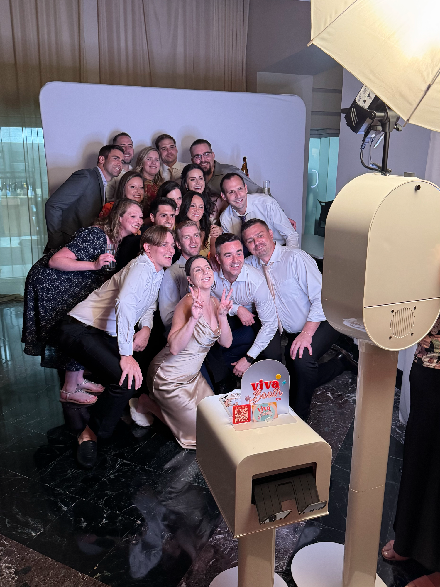 A large group of guests posing together in front of a white rounded backdrop beside the booth